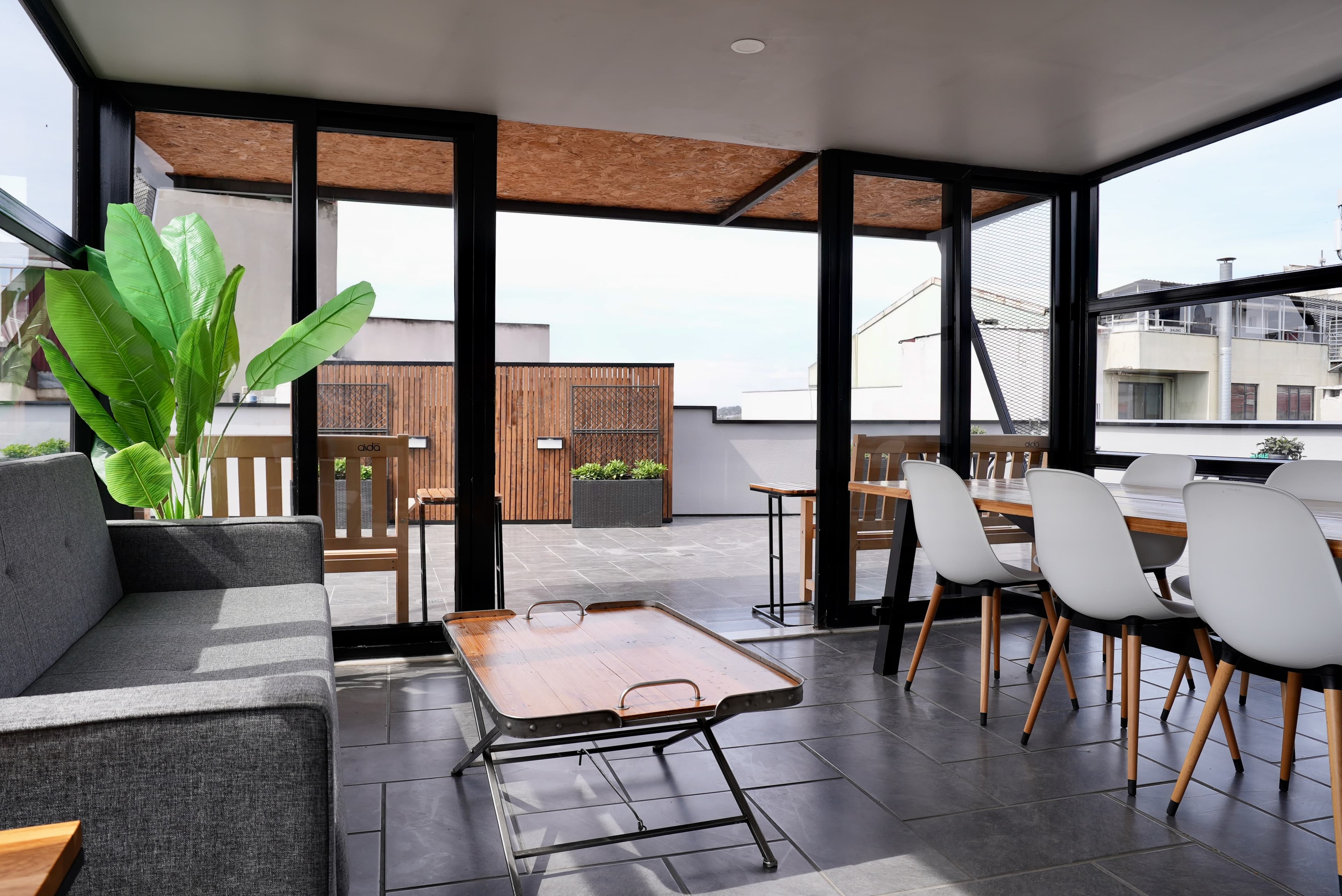 Rooftop sunroom with a sofa and a long table, opening onto the open deck