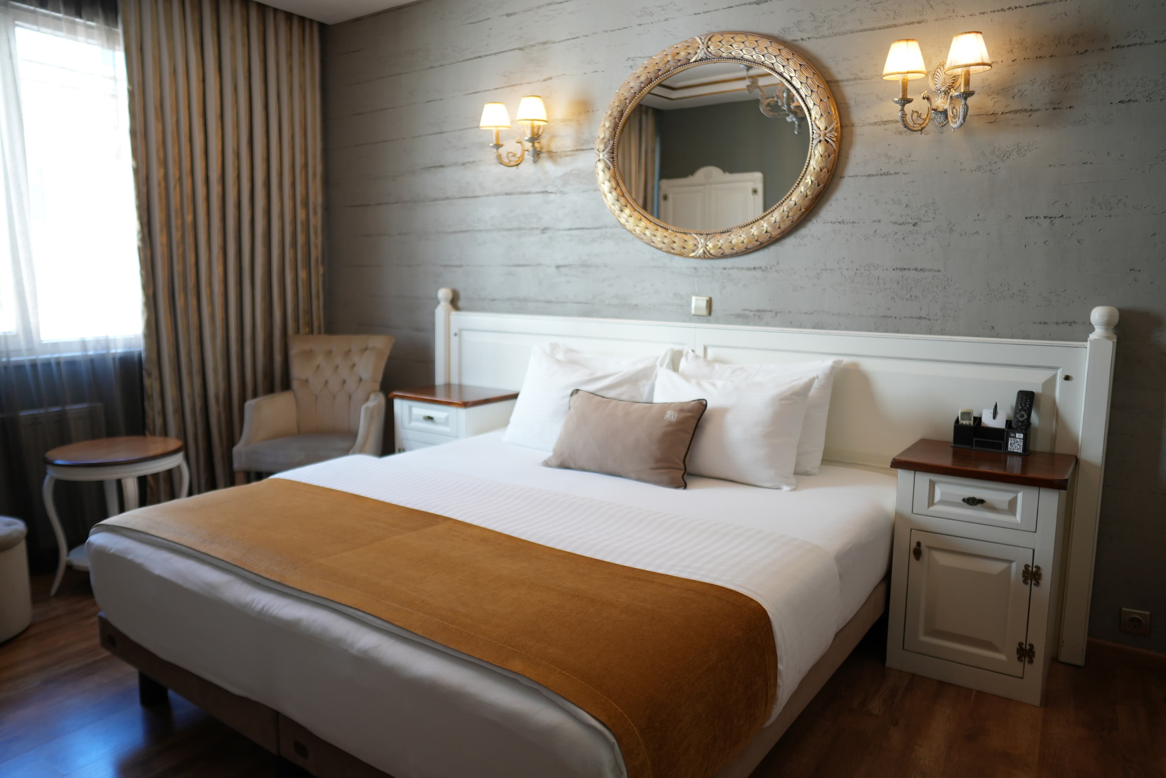 Suite main bedroom with a double bed, a gilded oval mirror and paired wall sconces