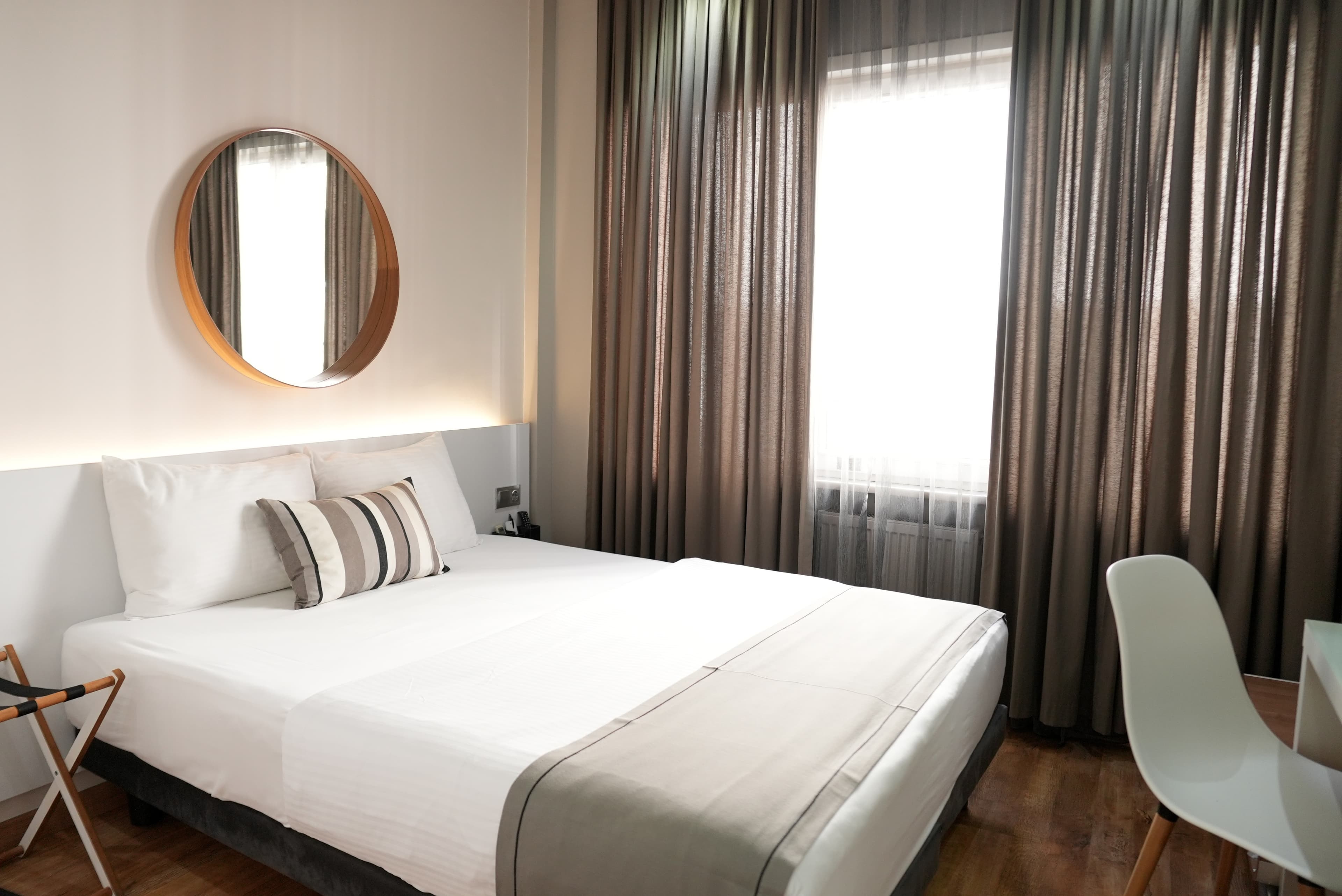 Standard double: double bed under a round mirror, with floor-length curtains and daylight from the window